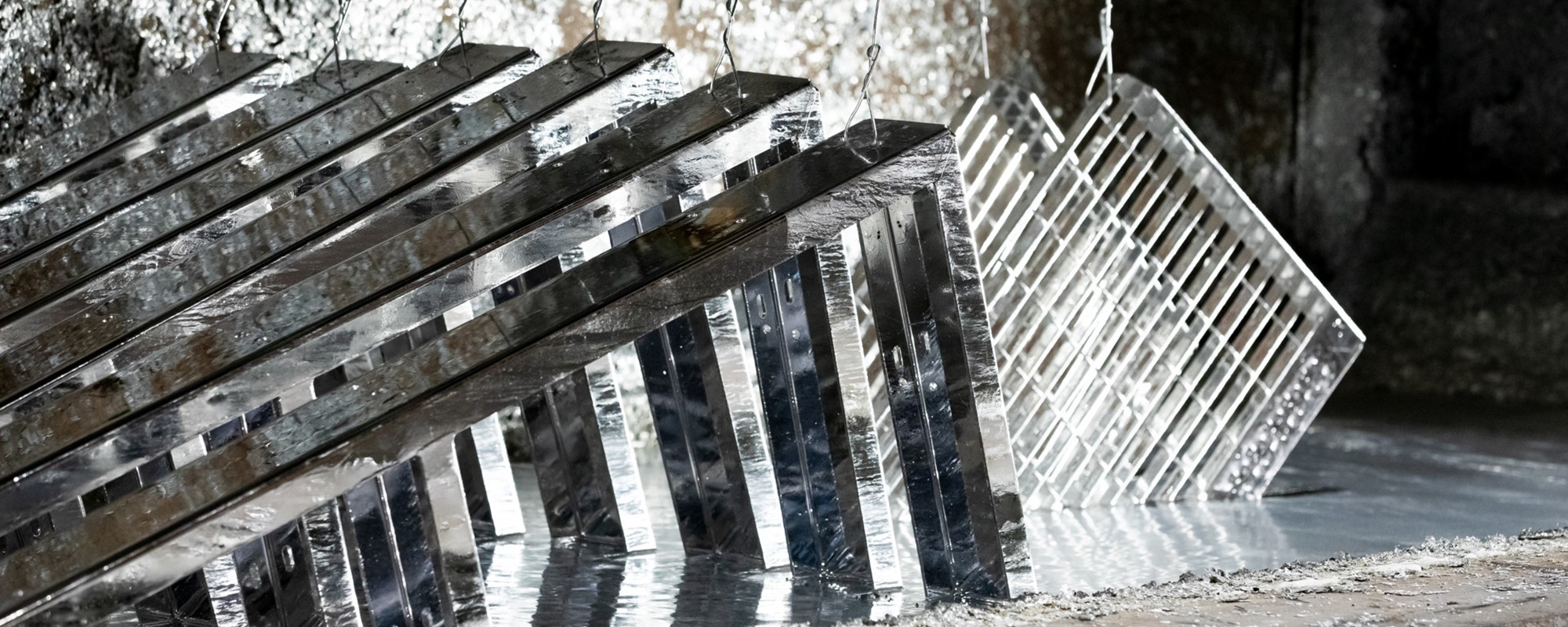 Gitterroste aus frisch feuerverzinktem Stahl werden nach dem Verzinkungsprozess aus dem Zinkbad gehoben – die silbrig glänzende Oberfläche zeigt die frische Zinkbeschichtung.